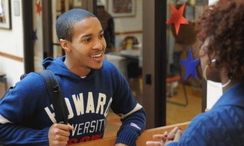 Image of Howard University student holding book bag and talking to a cafeteria service member